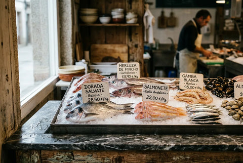 Mostrador de pescadería con pescado fresco sobre hielo y carteles de origen